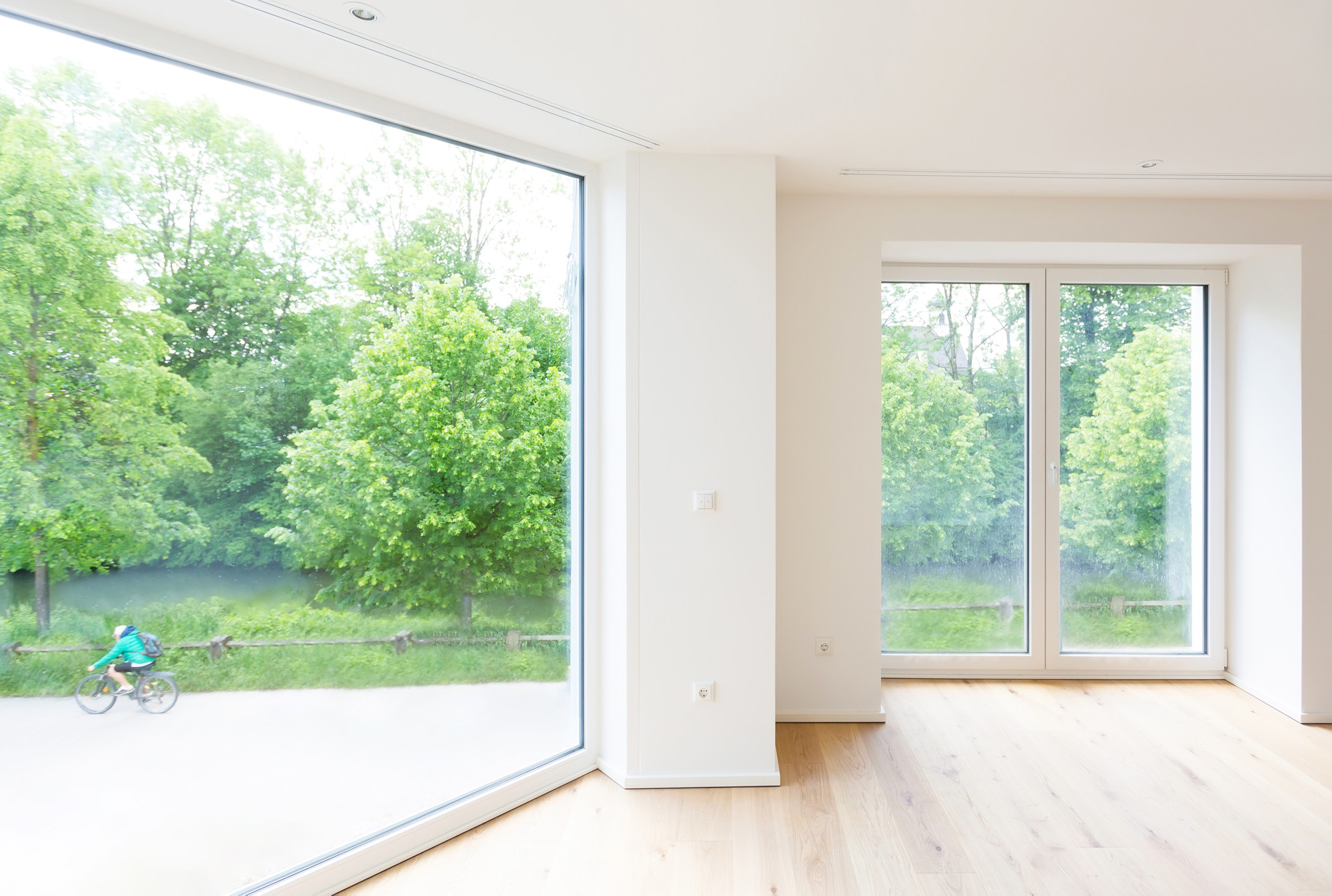 Architekturfotografie – Wohnraum für Moser Wohnbau Heller Wohnraum mit großen bodentiefen Fenstern, Holzboden und Blick ins Grüne – Architekturfotografie für Moser Wohnbau im Raum Rosenheim